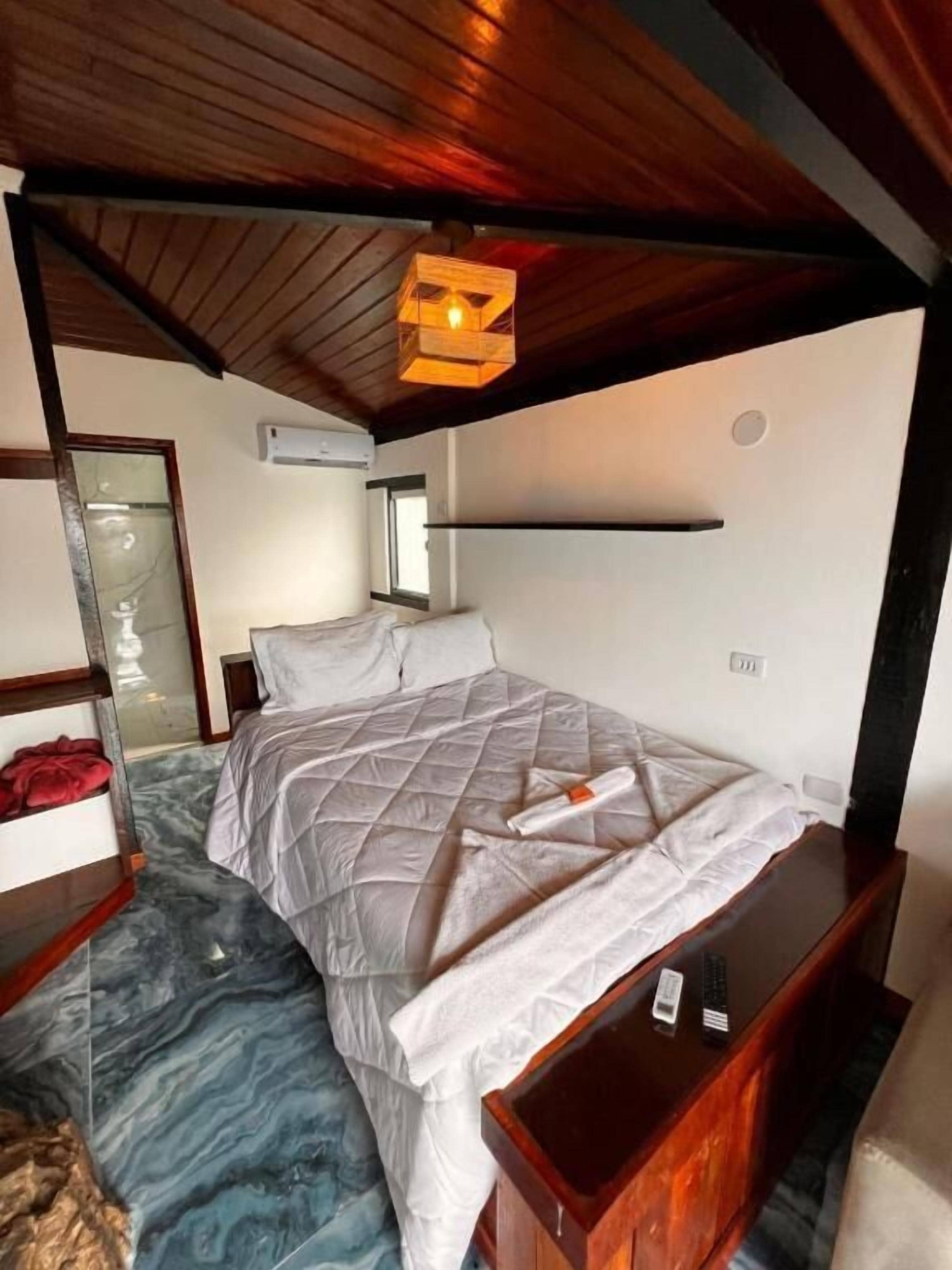 A bedroom with a bed, a wooden headboard, a marble floor, and a hanging light fixture.