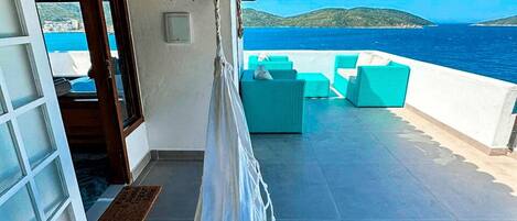 A terrace with a view of the sea, featuring a hammock, teal chairs, and a wooden door.