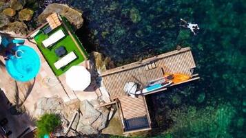 Una propiedad frente al mar con terraza de madera, piscina y muelle para barcos.