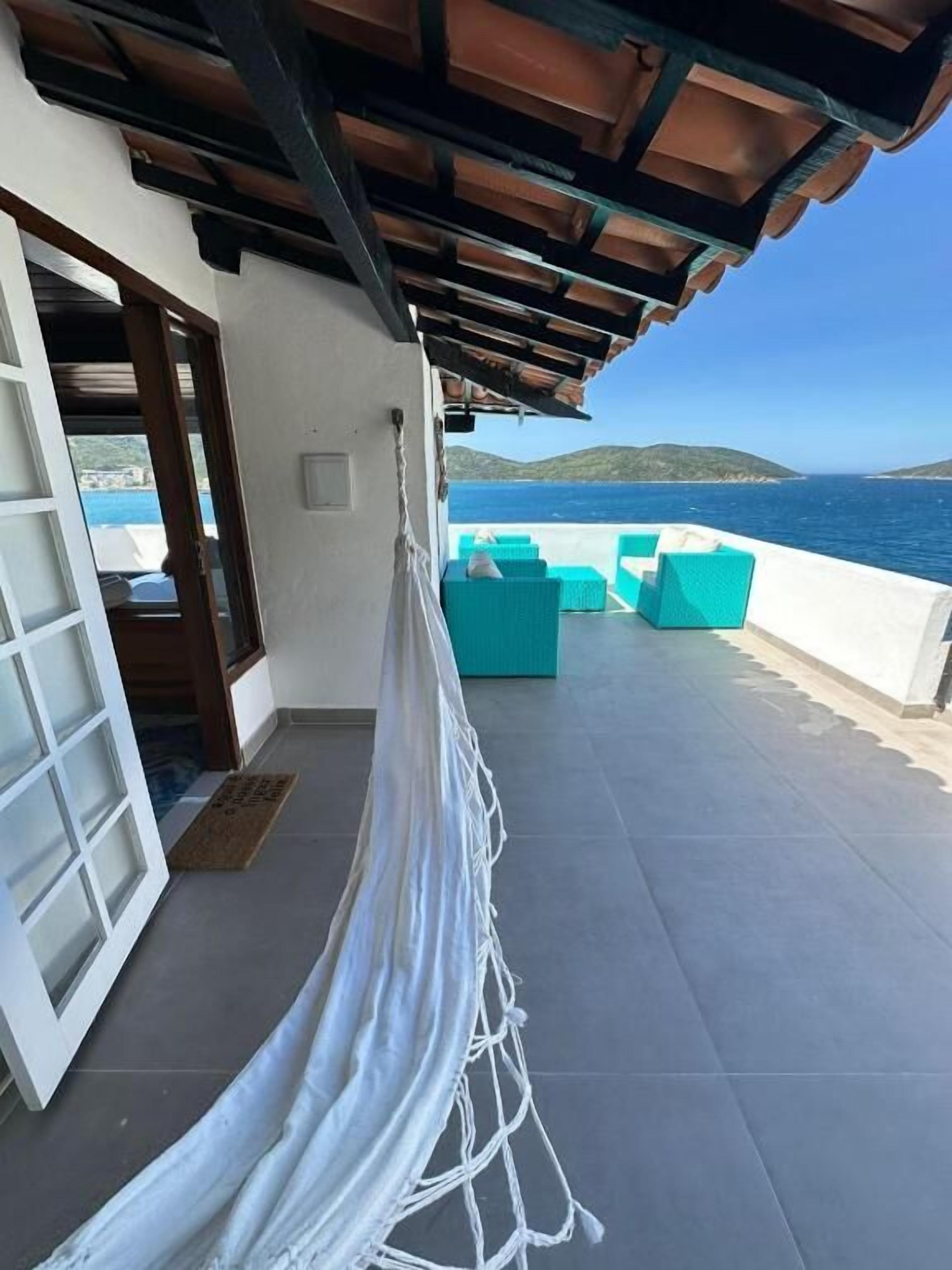 A balcony with a view of the sea, a hammock, and turquoise outdoor furniture.