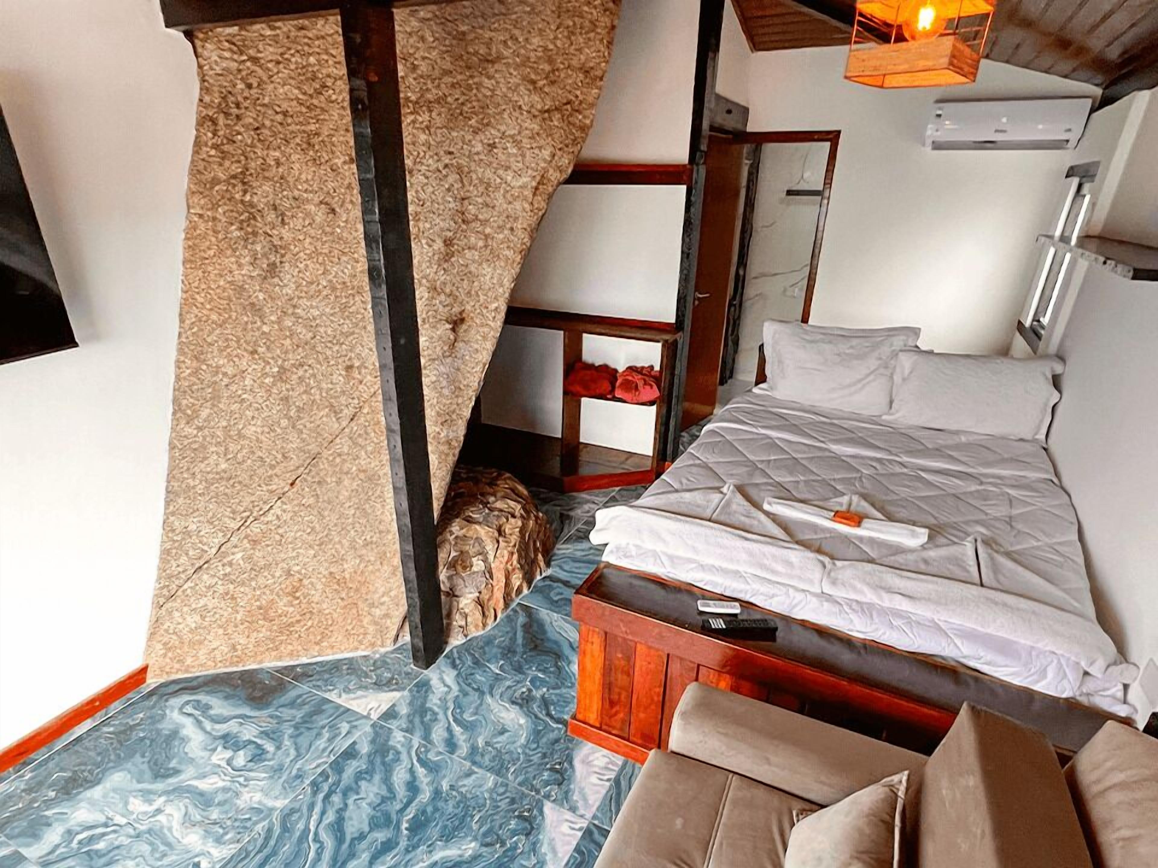 Un dormitorio con cama, una mesita de noche de madera, una silla roja y un estante pequeño con un objeto rojo.