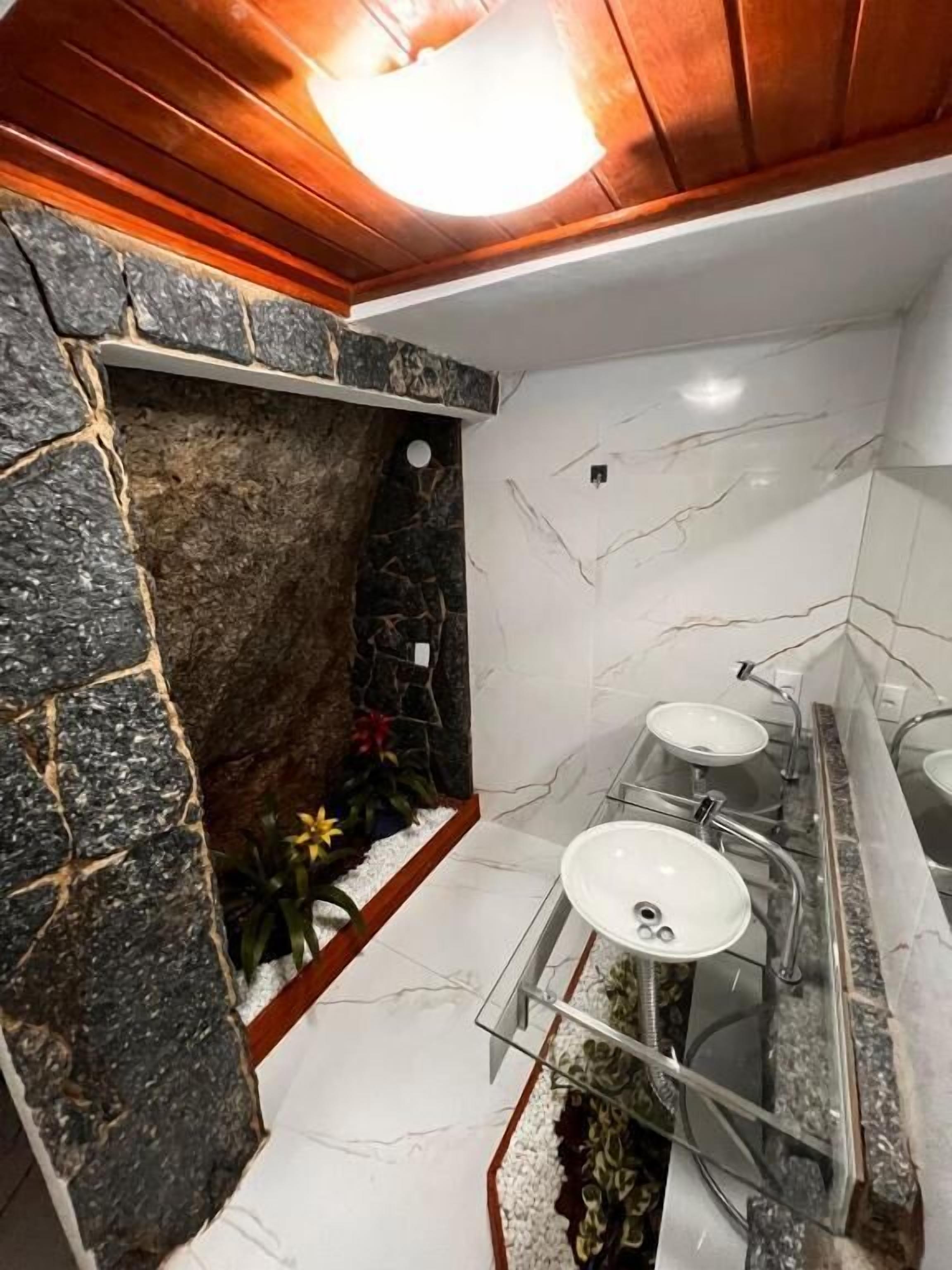 Une salle de bain avec un mur d’accent en pierre, une douche et un espace lavabo délimité par des parois en verre.