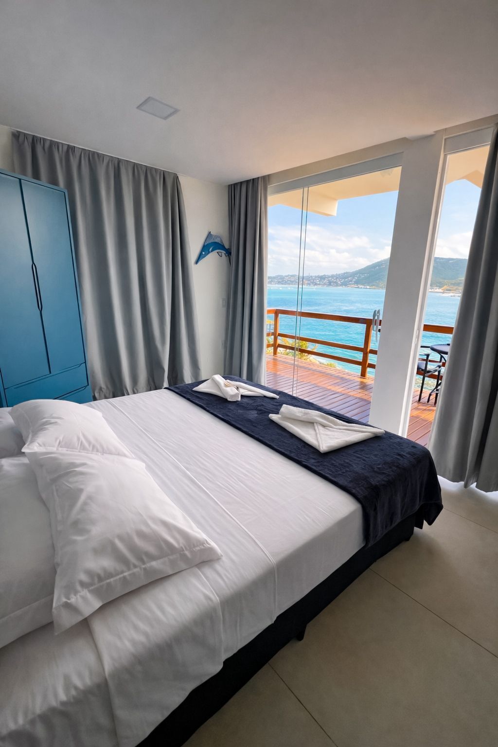 Une chambre d’hôtel avec un lit, une armoire bleue, un balcon donnant sur la mer et une table avec des chaises.