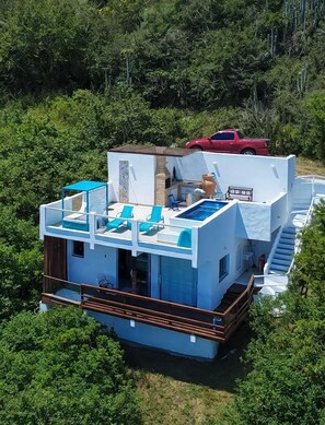 A modern house with a pool, a red truck parked nearby, and lush greenery surrounding it. - Pousada Vista Grega (Arraial do Cabo)