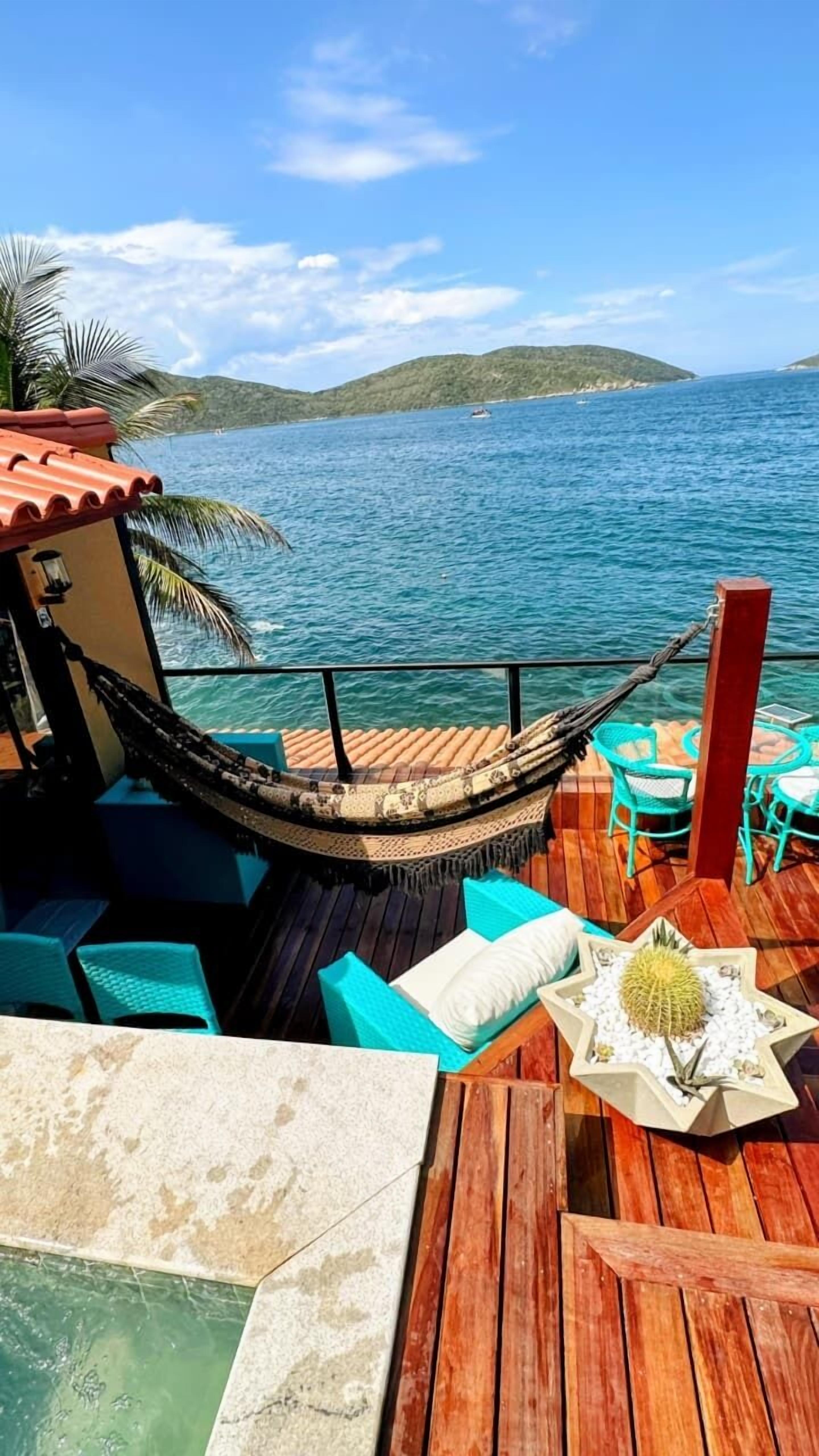 A wooden deck with a hammock, turquoise chairs, and a small table with a decorative centerpiece.