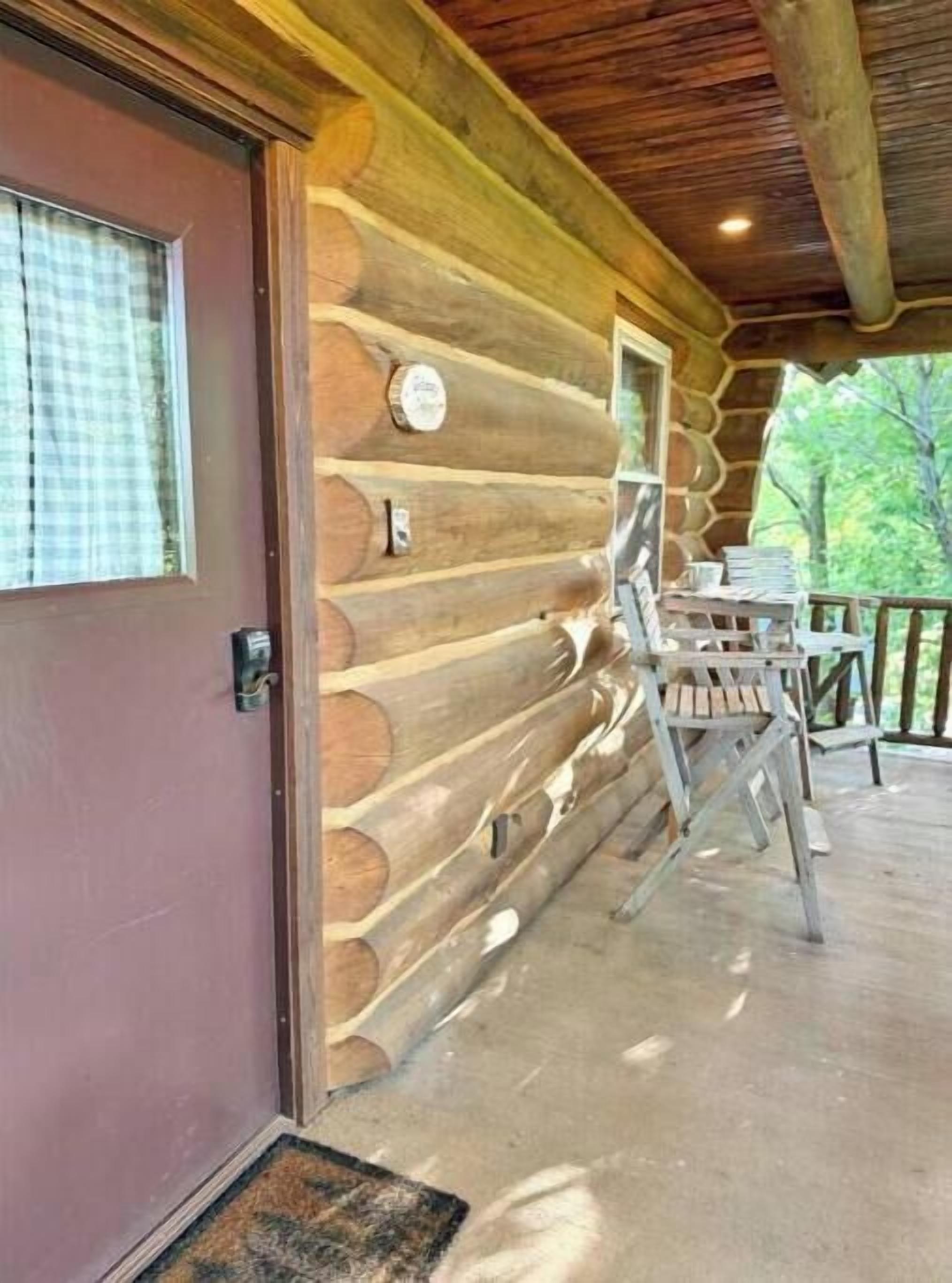 A log cabin with a wooden exterior, a door with a window, and a porch area with a table and chairs.