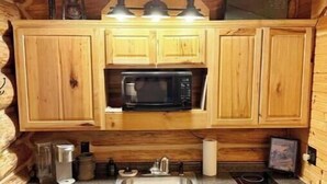 A compact kitchen with wooden cabinets, a stainless steel sink, a microwave, and a gas stove.