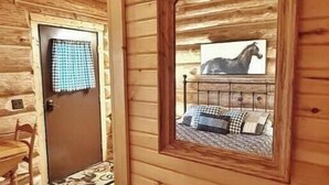A wooden cabin interior with a dining area, a door, and a mirror reflecting a bed with a horse picture.