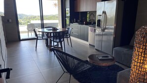 Eine moderne Küche mit einem großen Kühlschrank, einem Essbereich mit rundem Tisch und Stühlen sowie Blick auf eine gebirgige Landschaft durch große Fenster.