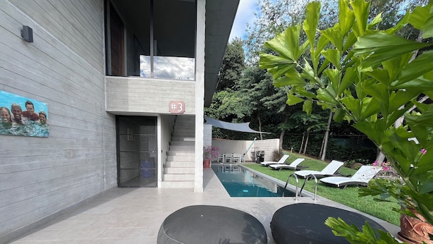 Ein moderner Poolbereich im Freien mit überdachter Sitzgelegenheit, einer Treppe und einem Wandgemälde.