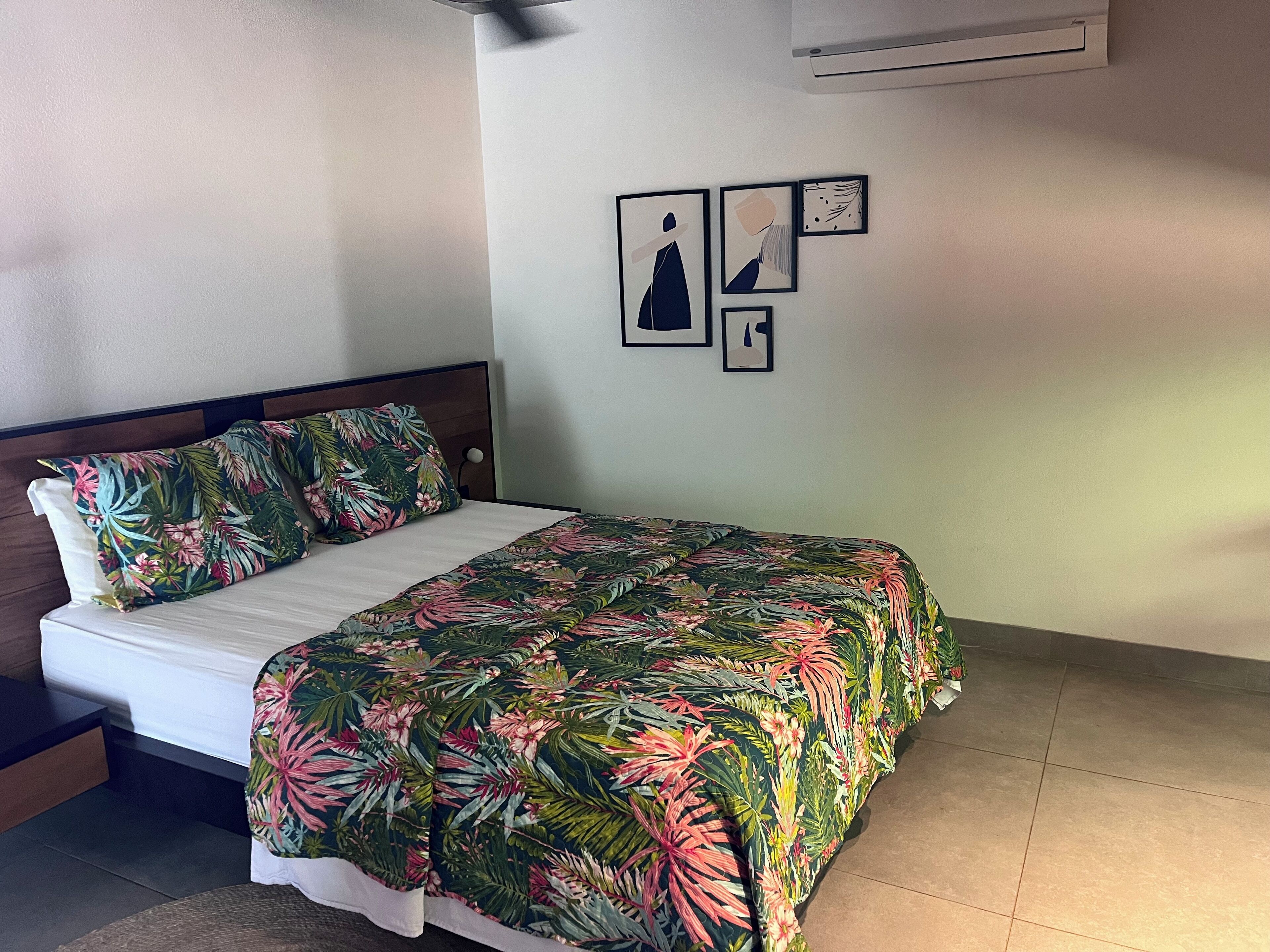 Ein Bett mit floralem Überwurf, einem Holzkopfende und einer Wand mit gerahmten Bildern.