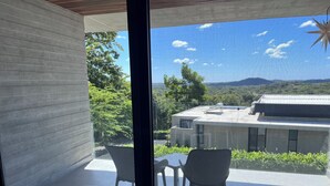 Ein modernes Zimmer mit Glastür, die auf einen Balkon mit zwei Stühlen und einem kleinen Tisch führt.
