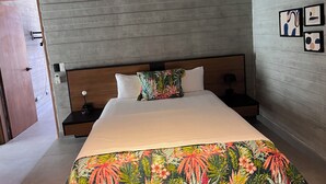 Ein Hotelzimmer mit Holz-Kopfteil, einem Bett mit floralem Überwurf, einem Nachttisch mit Lampe und einer Tür.