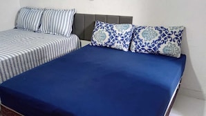 Dos camas con ropa de cama a rayas y azul, un cabecero gris y almohadas estampadas.