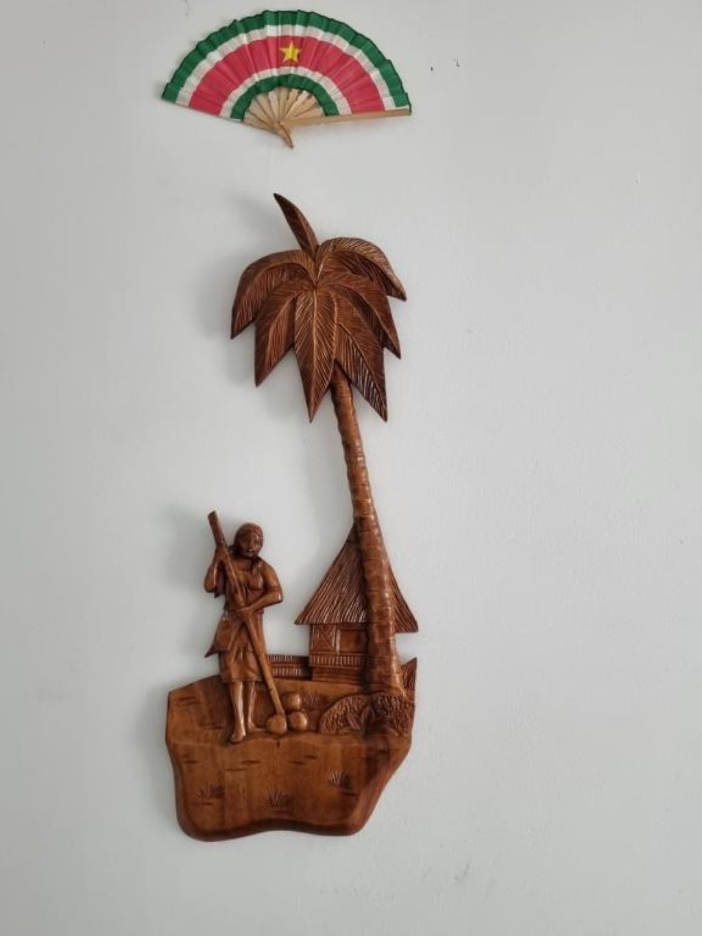 Eine Holzskulptur mit einer Palme, einer Person und einer Hütte.