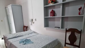 A bedroom with a bed, a chair, a wardrobe, and a shelf with decorative items. - Kwarts Appartementen - Standard Studio (Paramaribo)