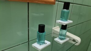 A bathroom with green tiles and two bottles of hand sanitizer mounted on a white holder. - Kwarts Appartementen - Standard Studio (Paramaribo)