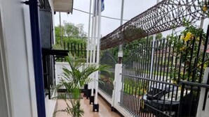 A balcony with a tiled floor, a white table, a chair, potted plants, and a metal fence. - Kwarts Appartementen - Standard Studio (Paramaribo)