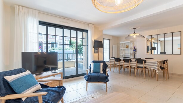 A spacious living room with a large TV, a dining area with a table and chairs, and a large window with a view of the outside. - Proche mer très agréable appt de 2 ch pour 5 pers (Le Touquet-Paris-Plage)