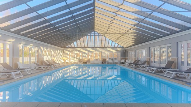 Ein Innenpool mit Glasdach, sonnendurchflutete Räume und Liegestühle am Pool.