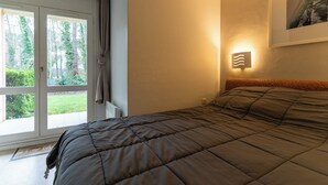 Ein Schlafzimmer mit einem großen Bett, einem Fenster mit Vorhängen, einer Wandleuchte und einem gerahmten Bild.