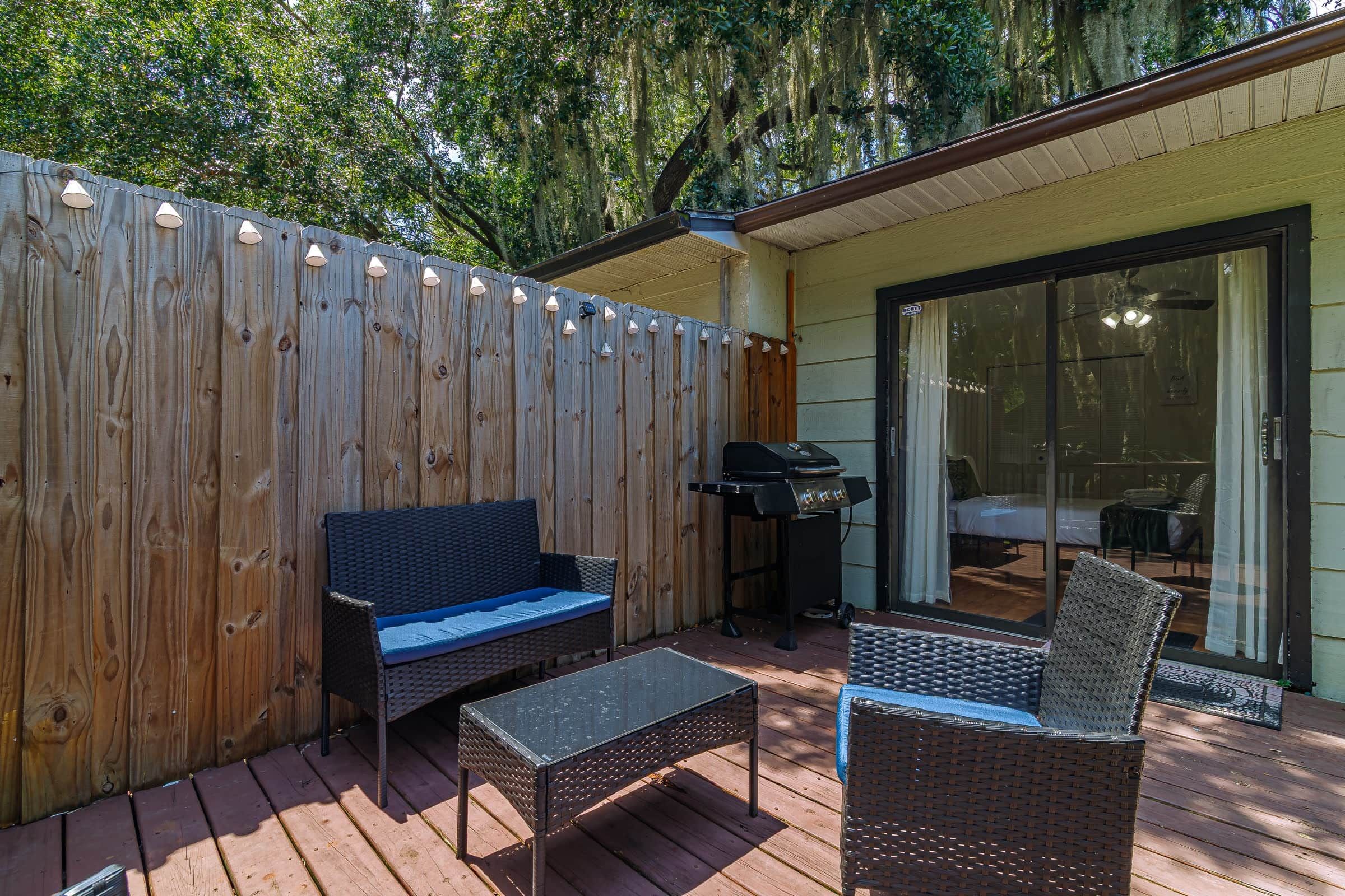 An outdoor patio with a wooden deck, a black grill, a blue sofa, and wicker chairs.