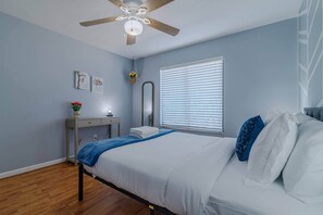 A bedroom with a bed, a desk, a mirror, and a ceiling fan.