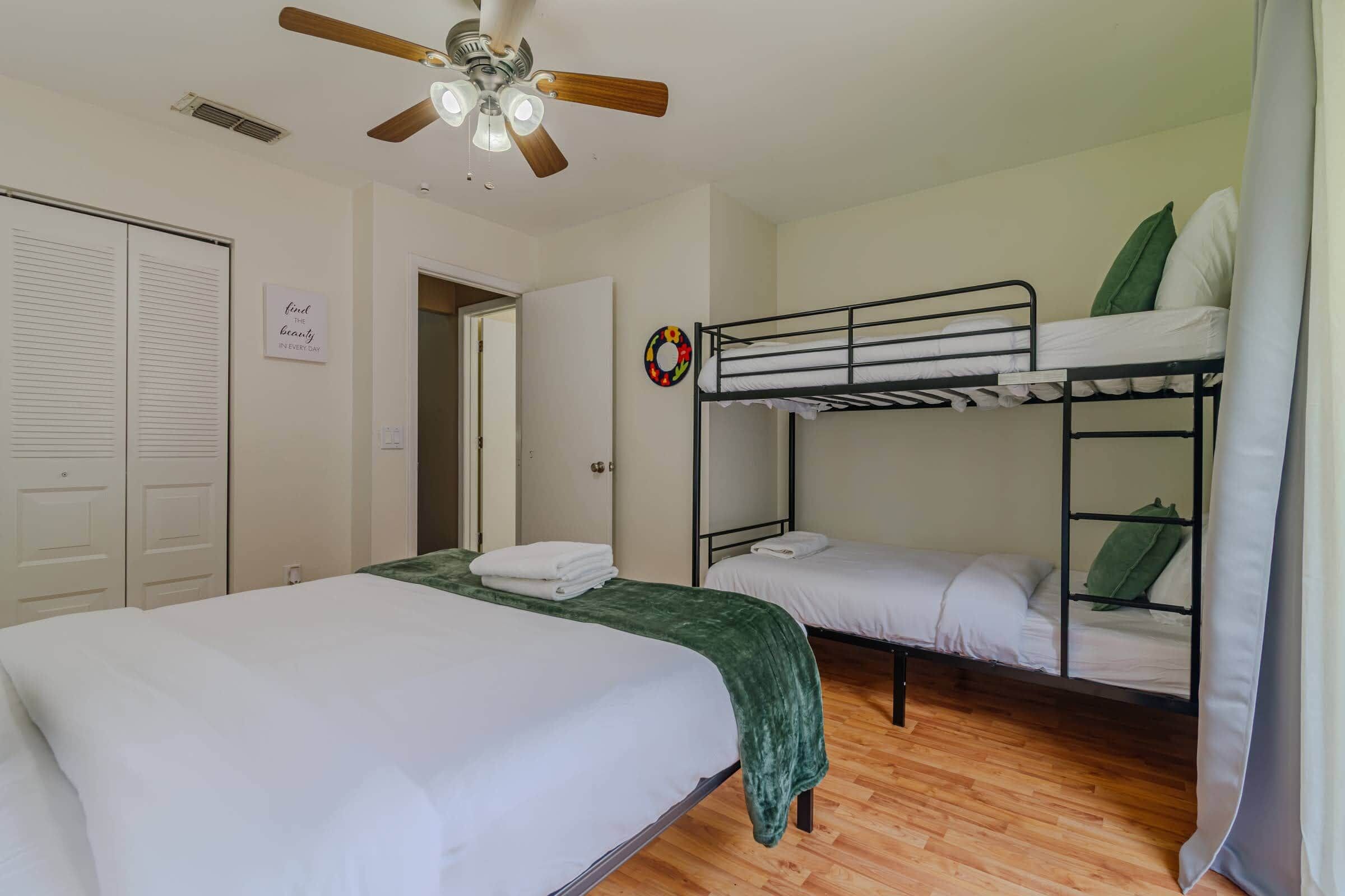 A dormitory room with bunk beds, a ceiling fan, a door with a sign, and a wall decoration.