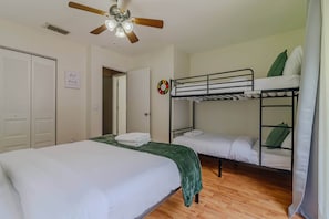 A dormitory room with bunk beds, a ceiling fan, a door with a sign, and a wall decoration.