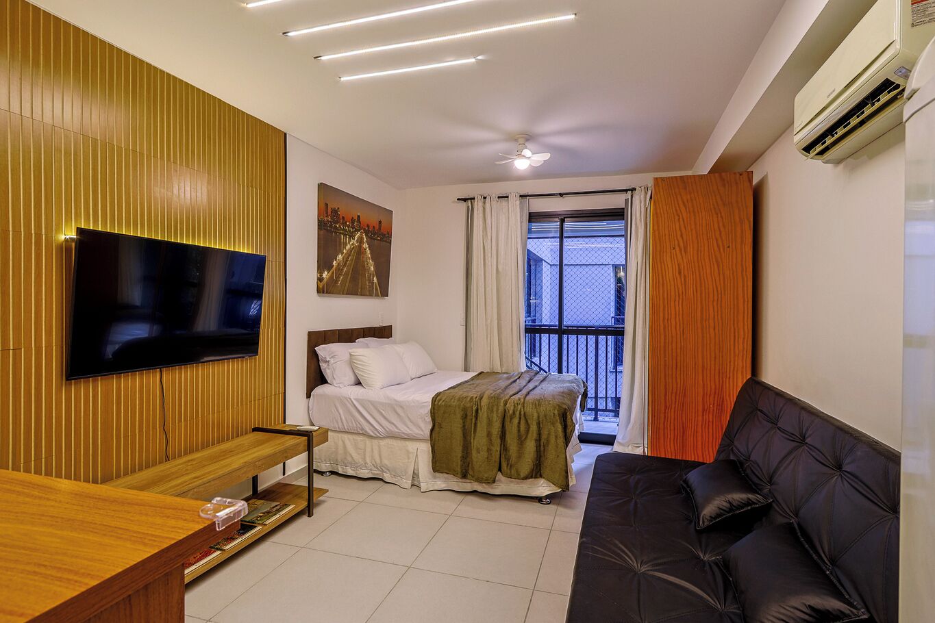 A modern bedroom with a bed, a TV mounted on the wall, a ceiling fan, and an air conditioning unit.