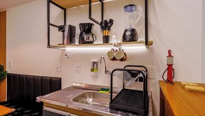 Una cocina compacta con un lavamanos, una cafetera, una licuadora y una estufa a gas roja.