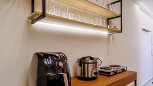 Una zona de cocina con cafetera, olla de cocción lenta y estante de madera con vasos de vidrio.