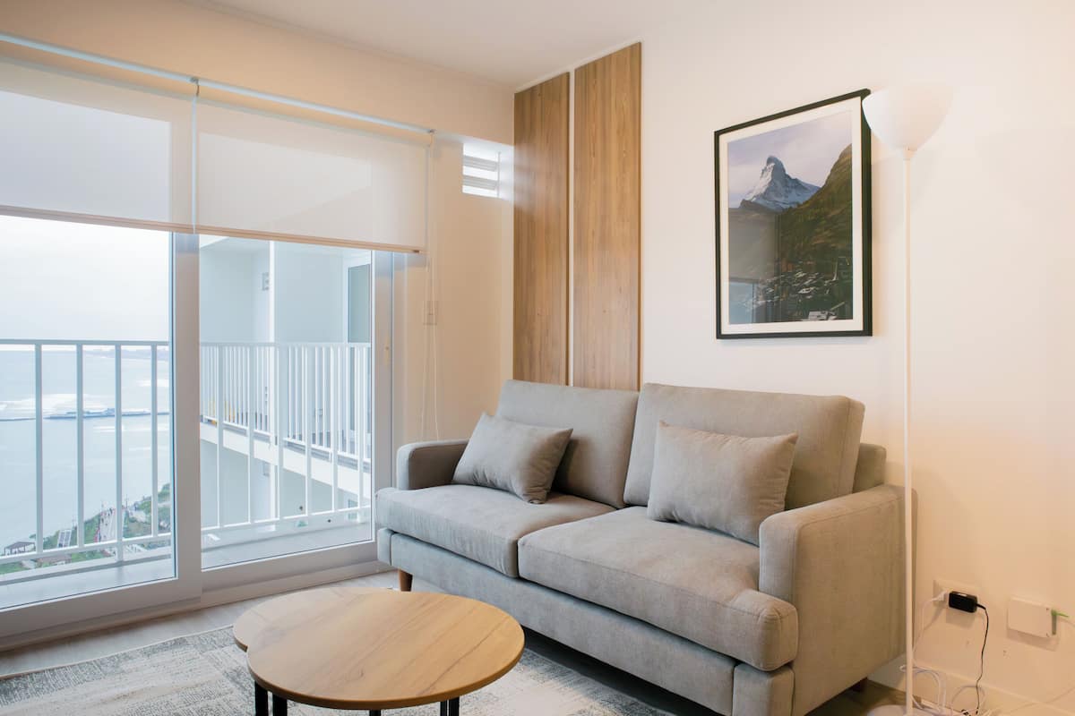 A modern living room with a sofa, a coffee table, and a large window offering a view of a balcony.