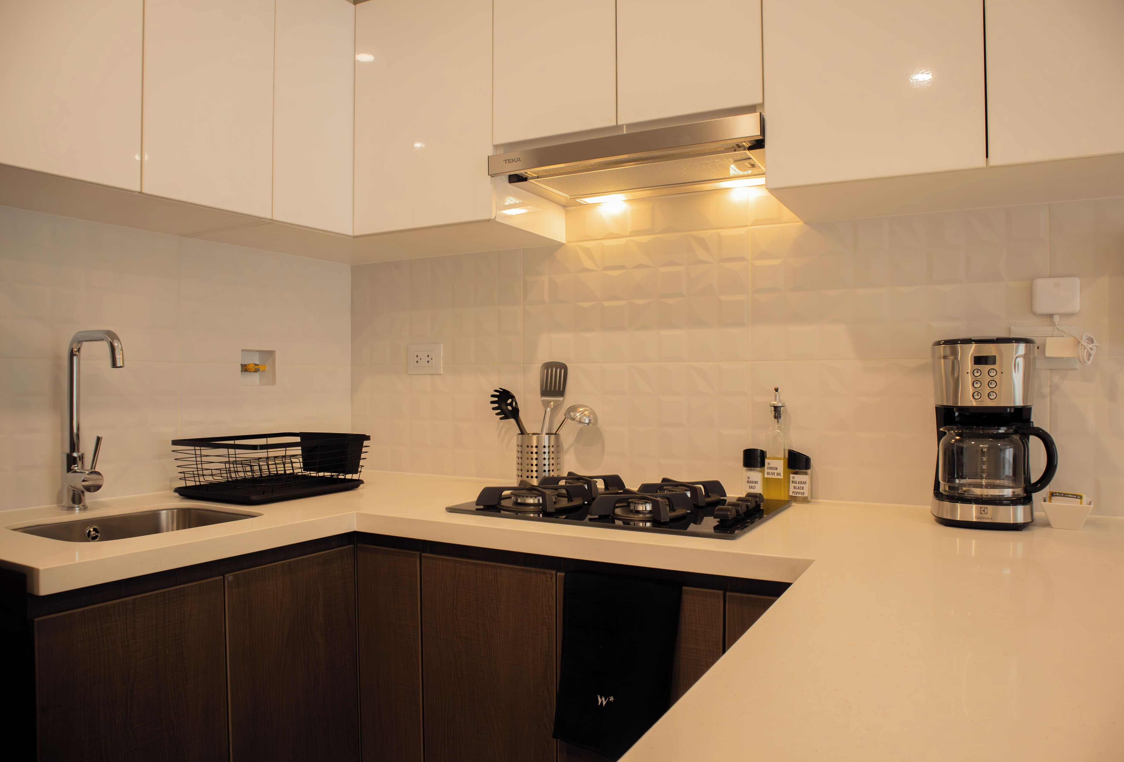 A modern kitchen with white cabinets, a stainless steel sink, a gas stove, and a coffee maker.