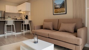 Ein modernes Wohnzimmer mit einem beigen Sofa, einem weißen Couchtisch und einer Küchenzeile im Hintergrund.
