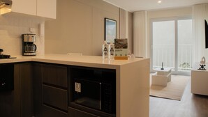 Eine moderne Küche mit integriertem Mikrowellenherd, einer Kaffeemaschine und einem Kühlschrank. Ein großes Fenster bietet einen Blick ins Freie.