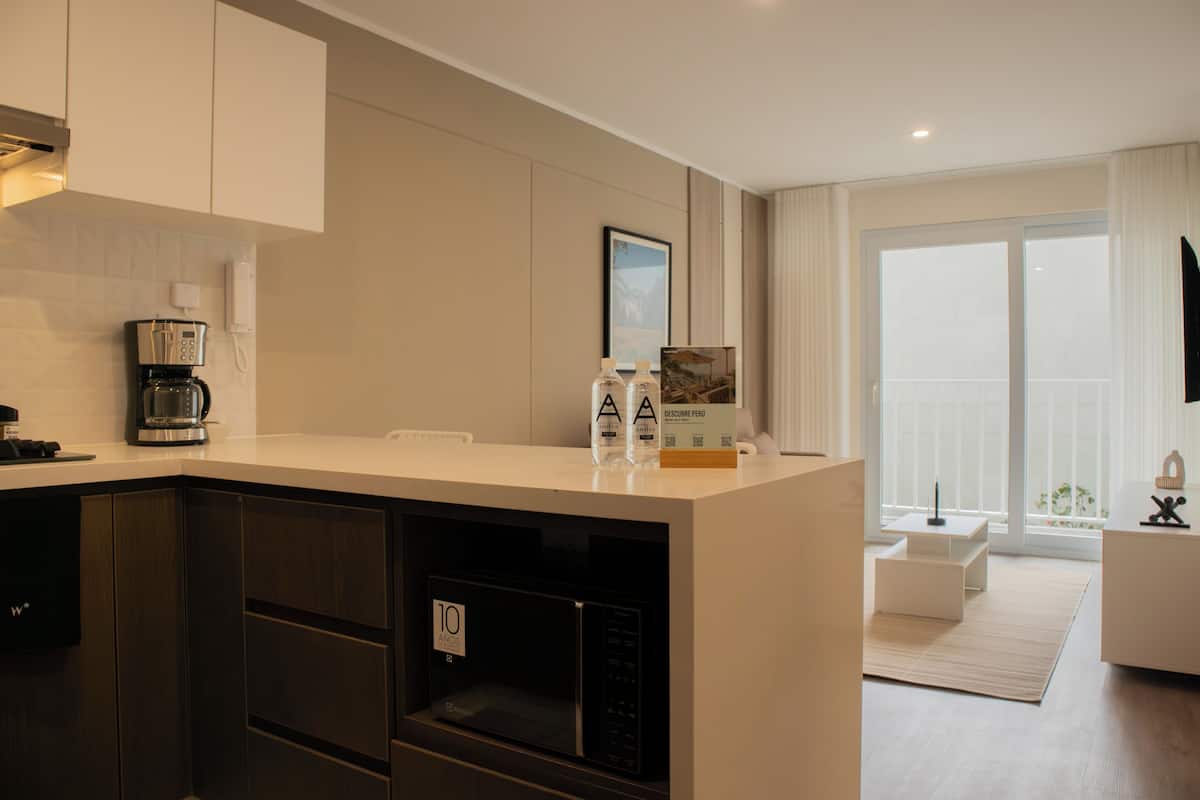 A modern kitchen with a built-in microwave, a coffee machine, and a refrigerator. There is a large window providing a view of the outdoors.