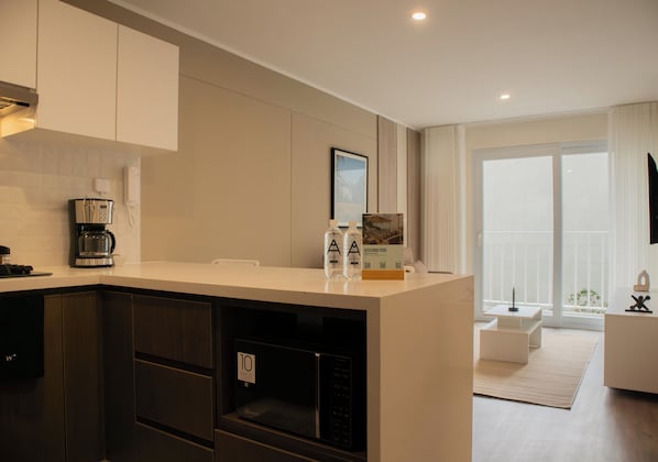 A modern kitchen with a built-in microwave, a coffee machine, and a refrigerator. There is a large window providing a view of the outdoors. - Sight by Wynwood House (Lima)