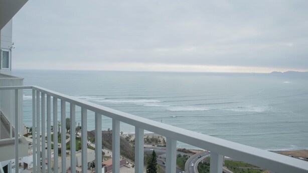 Ein Balkon mit Blick auf das Meer und eine Straße mit Fahrzeugen.