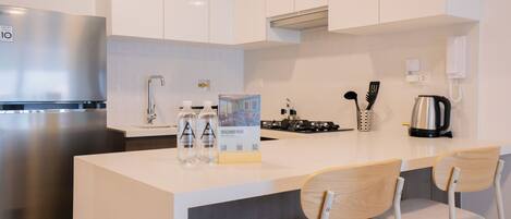A modern kitchen with a stainless steel refrigerator, a gas stove, and a coffee maker. There are two chairs with wooden seats and metal frames.