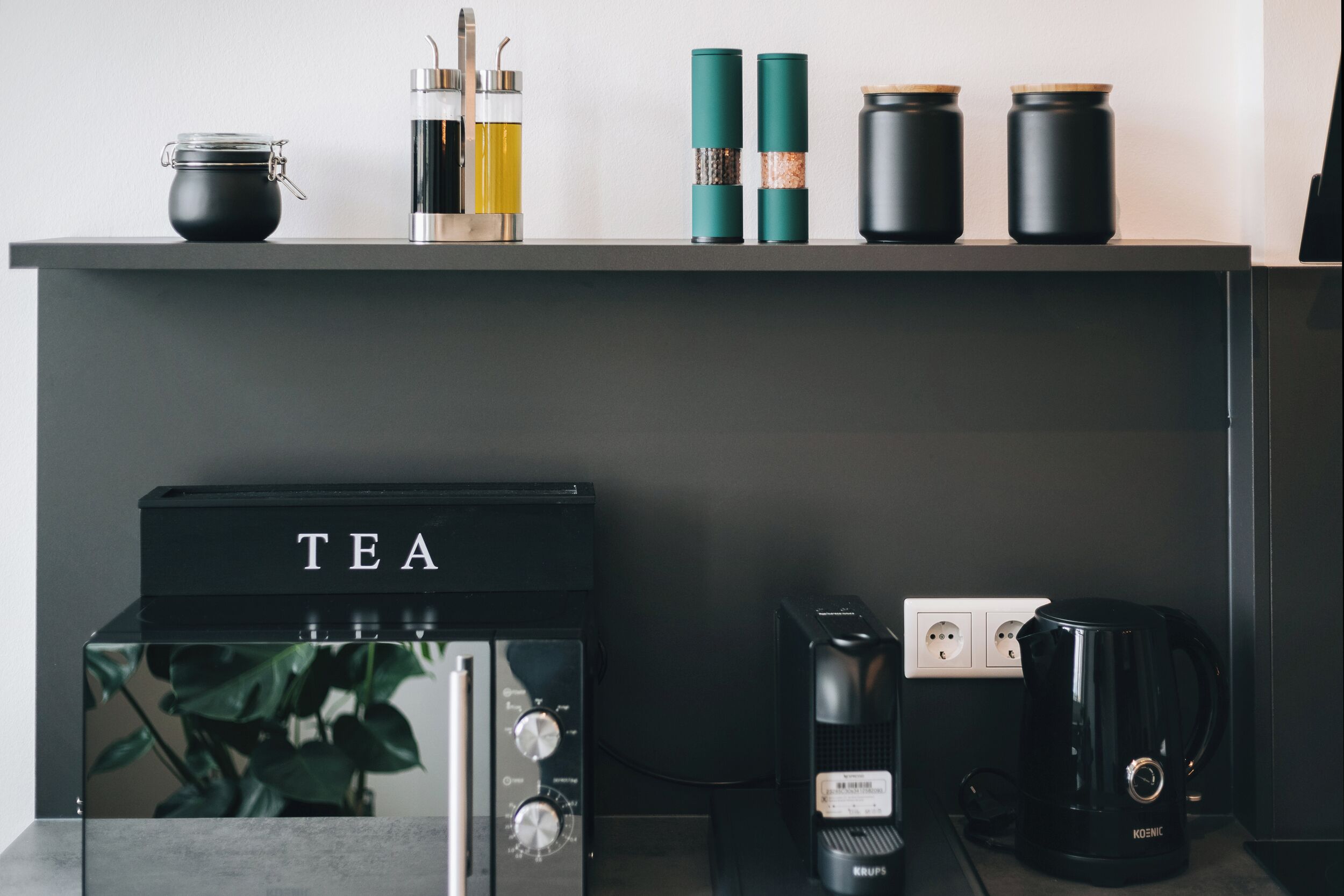 Eine Küche mit einer Kaffeemaschine, einem Wasserkocher und verschiedenen Behältern auf der Arbeitsplatte.