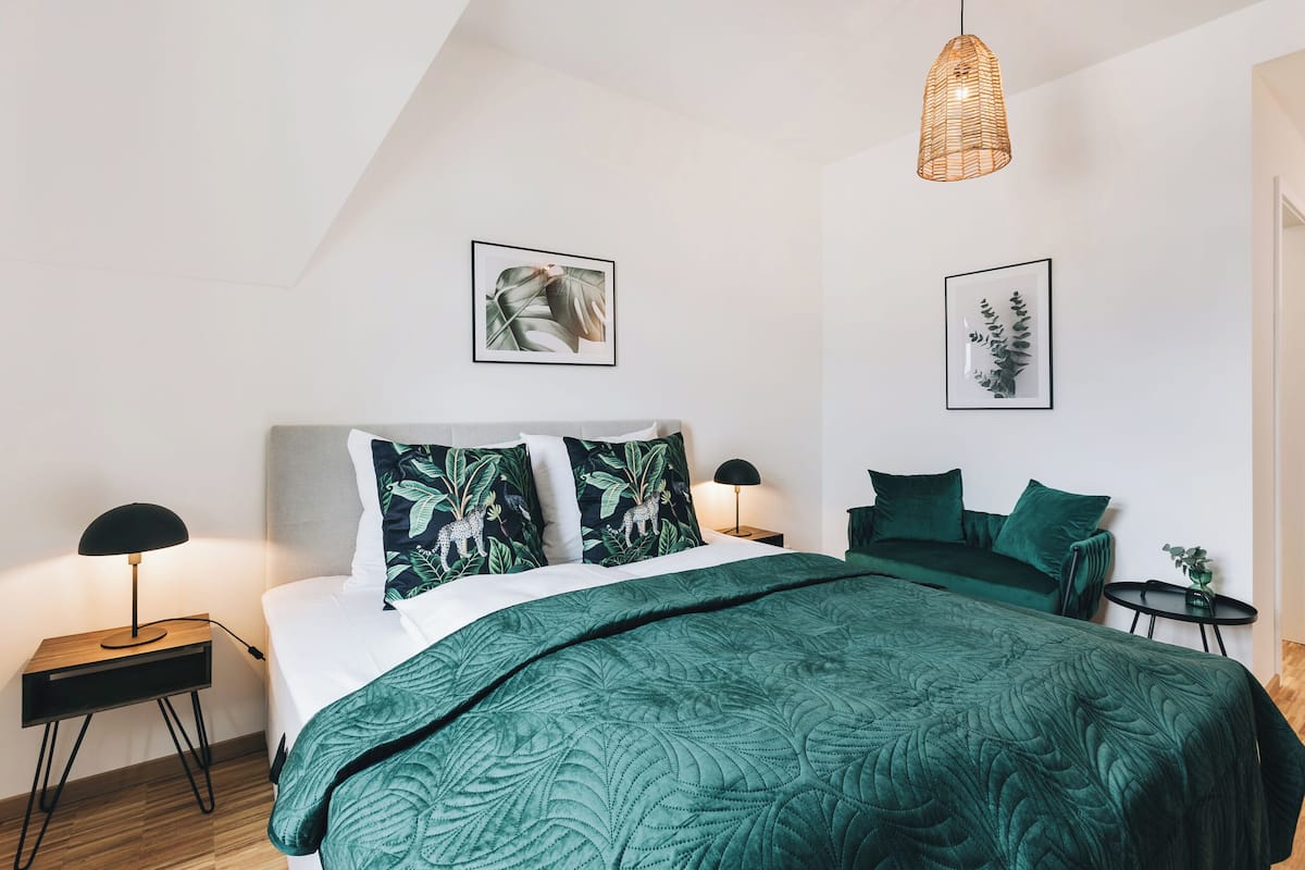 A modern bedroom with a large bed, green bedding, and two wall-mounted lamps.