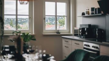 A kitchen with a view of a town through a window, a coffee machine, and a plant.