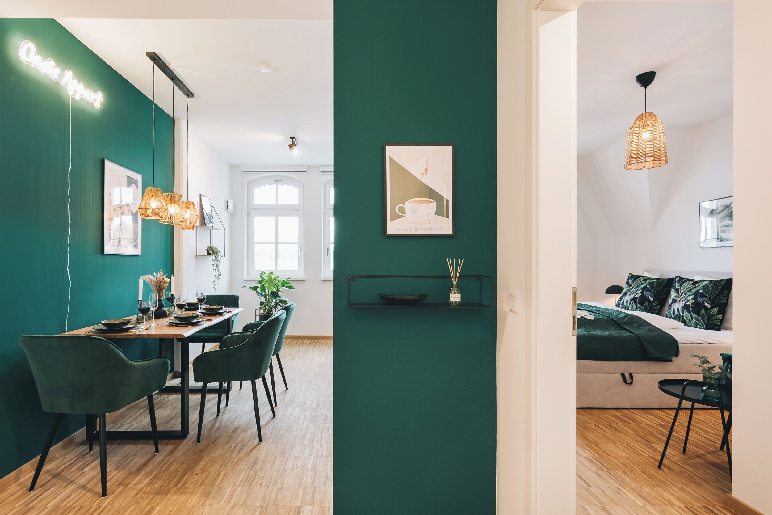 A modern interior with a dining area, a green accent wall, and a cozy seating area with a bed.