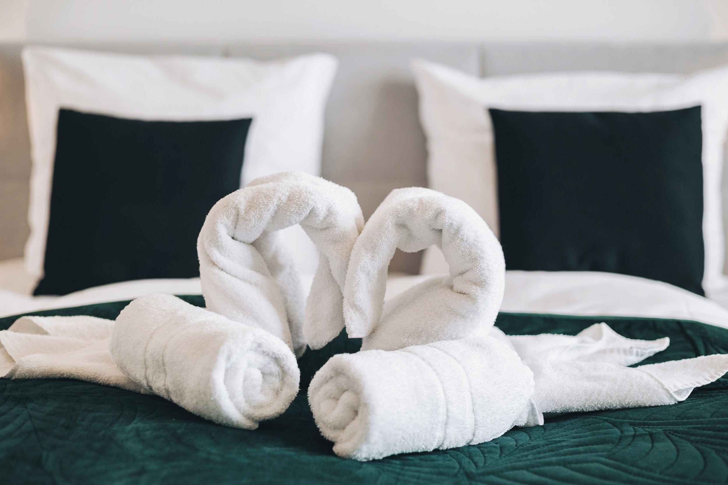 A bed with white towels arranged in a heart shape on a green bedspread.