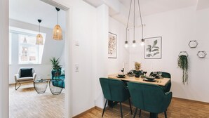 A modern dining area with a wooden table, green chairs, pendant lights, and wall art. - Oasis Appart - Wohnen in Dresden (Dresden)