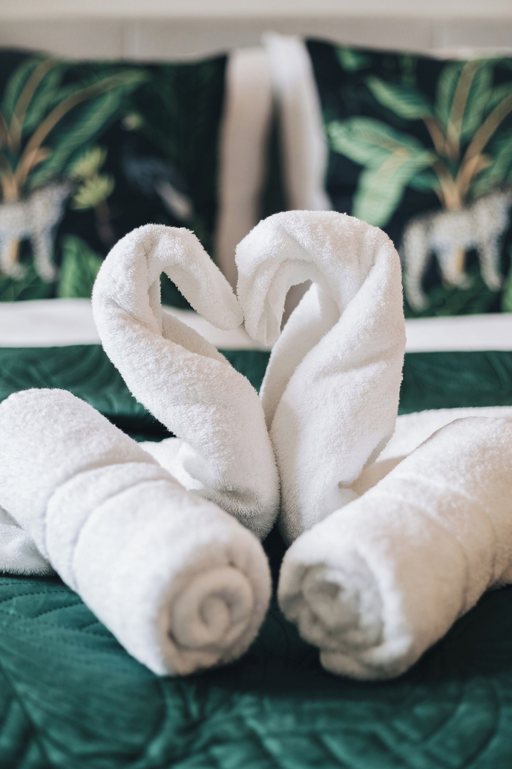 Un letto con biancheria verde e due asciugamani bianchi disposti a forma di cuore.