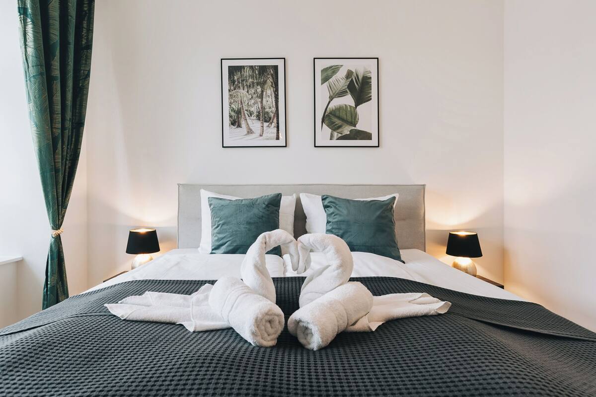 A neatly made bed with two pillows, two wall-mounted pictures, and two bedside lamps.