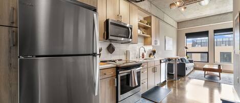A modern kitchen with stainless steel appliances, wooden cabinets, and a large window providing natural light.
