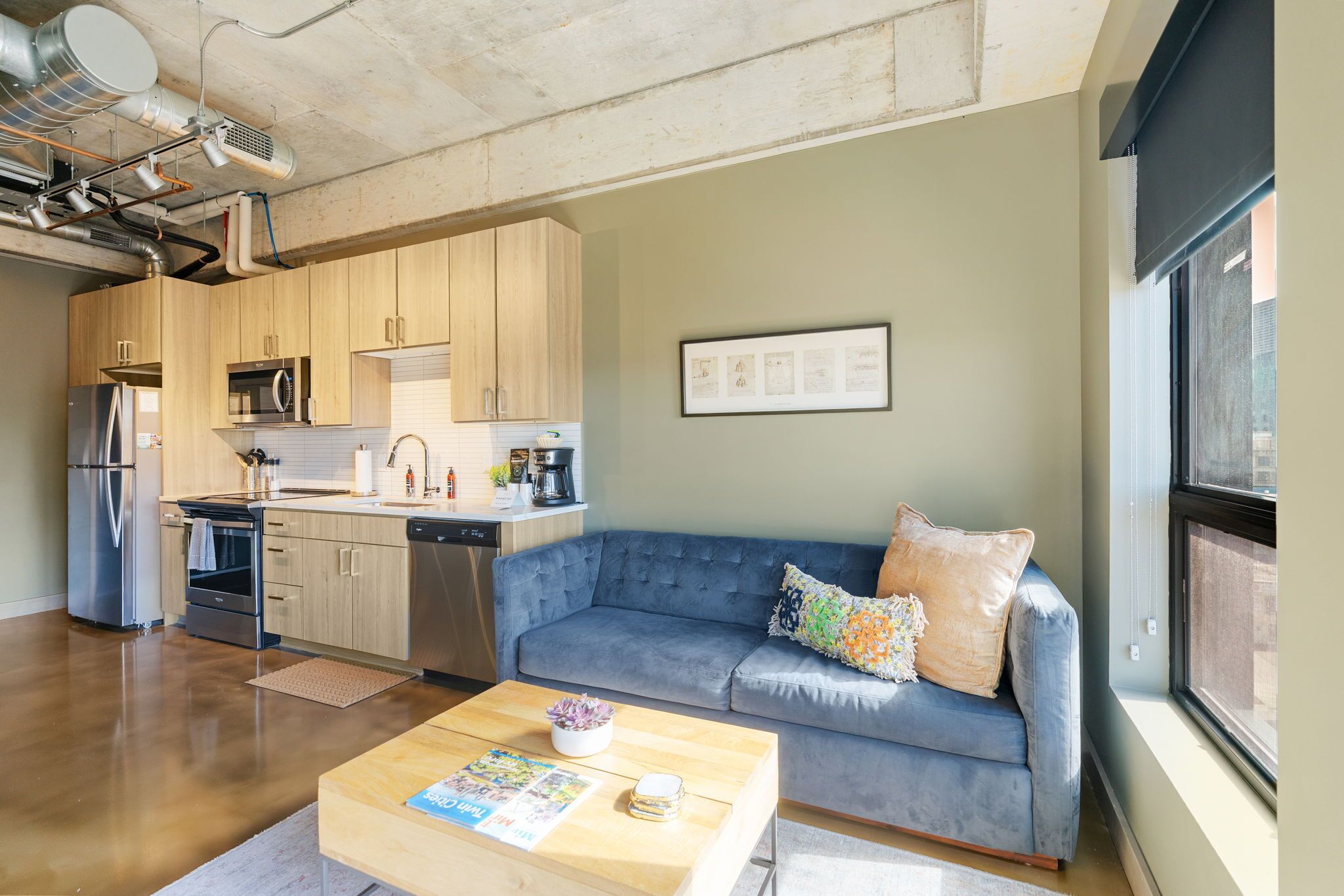 Una cocina moderna con electrodomésticos de acero inoxidable, un sofá azul y una mesa de centro con una revista.
